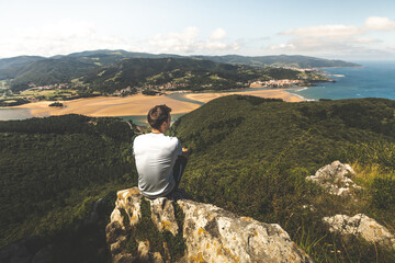 Young caucasian man on the top of a mountain looking to Urdaibai rivermouth next to the Cantabric...