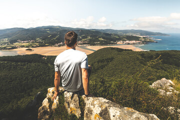 Young caucasian man on the top of a mountain looking to Urdaibai rivermouth next to the Cantabric sea, at Bizkaia; Basque Country.