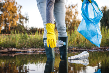 Environmental damage. Volunteer picking up plastic bottle from polluted river or lake. Water...