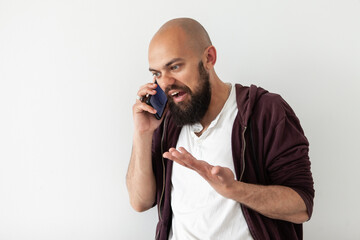 Irritated bearded bald handsome man emotionally talking on the phone on a white background. Proves his point