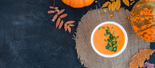banner with flat lay of pumpkin soup next to yellow leaves, pumpkins and napkin on black texture background. warming hearty soup on a cold autumn day. rustic style