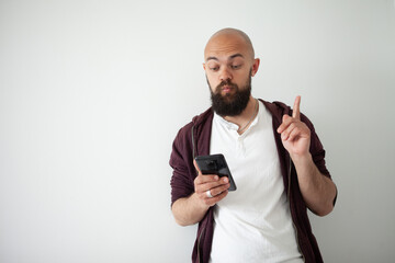 Bearded man using smartphone standing over isolated white background surprised with an idea or question pointing finger