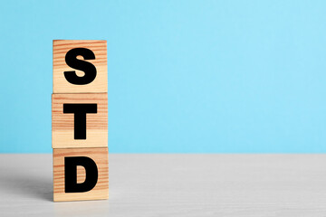 Abbreviation STD made with cubes on white wooden table against light blue background, space for text