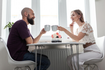 Cute couple are drinking coffee or tea in the kitchen. Husband and wife spend time together.