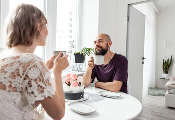 Cute couple are drinking coffee or tea in the kitchen. Husband and wife spend time together.