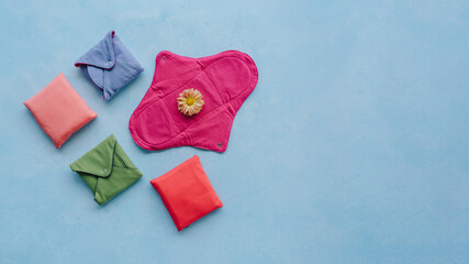 Cotton sanitary pads that are washable, reusable, biodegradable, eco friendly. Colorful pads against blue textured background with copy space