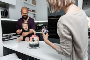 Birthday. Happy family concept. Young mother takes pictures of her daughter and husband with a cake in kitchen