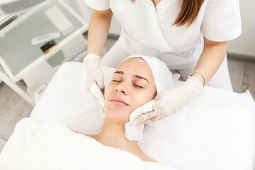 Fototapeta na wymiar Facial massage and skincare treatment. Dermatologist hands cleaning relaxed serene young woman face with napkin in beauty salon during skincare treatment.
