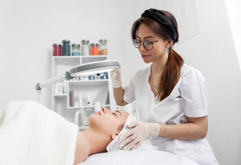 Skincare treatment. Dermatologist carefully examines the client's face before the cosmetic procedure in beauty salon