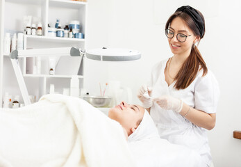 Fototapeta premium Cute woman beautician makes a cosmetic procedure to a patient in a beauty salon. Facial skin care