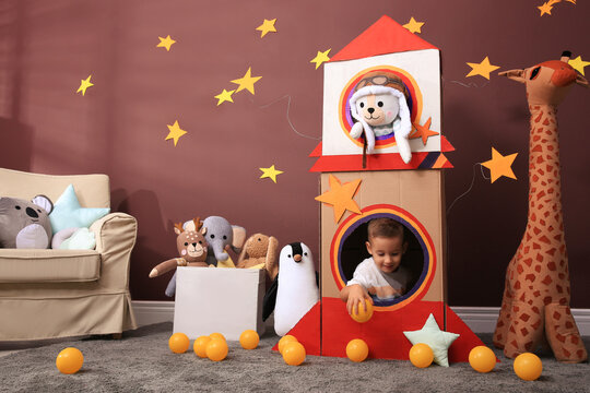 Cute little boy playing with cardboard rocket and toys at home. Child's room interior