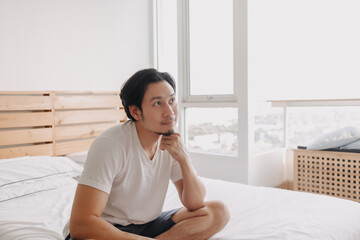 Happy Asian man sits and relax on his bed in his apartment.