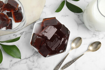 Delicious grass jelly cubes, milk and green leaves on white marble table, flat lay