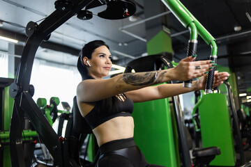 Fototapeta na wymiar Young fitness woman exercising pectoral muscles doing hand reduction in exercise machine in gym