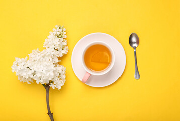 Cup of black aromatic tea with lemon and branches of blooming lilacs on yellow background. Top...