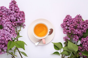 Cup of black aromatic tea with lemon and branches of blooming lilacs on white background. Top view. Flat lay