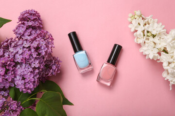 Obraz na płótnie Canvas Nail polish bottles with branches of blooming lilacs on pink background. Spring, beauty concept. Top view. Flat lay