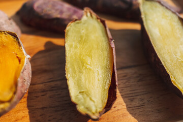 Cooked sweet potato cut into half on wooden plate.