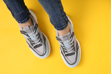 Female legs in fashionable jeans and sneakers on yellow background