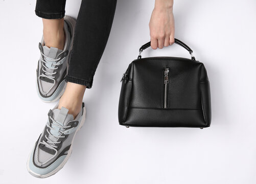 Woman in sneakers holds a black leather bag on a white background. Top view. Crop photo
