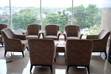 Yogyakarta, Indonesia, Oct 5, 2021. Set of chairs and tables for guests or visitors to relax in a hotel lobby with a large glass window as the background. 