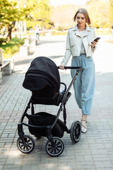 Stylish mom with stroller using smartphone in autumn park