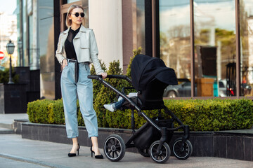 Stylish loving mom walks with a stroller in the city location. Maternity, lifestyle