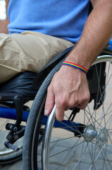 Obraz premium man hand in wheelchair with rainbow LGBTQ bracelet vertical