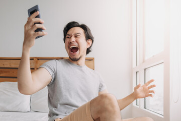 Shocked and happy Asian man get good news from the smartphone.