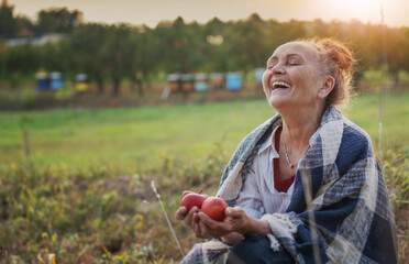 Fototapeta premium Cheerful happy mature senior woman holding red apples sitting in her garden