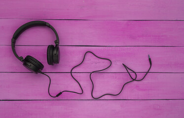 Stereo headphones with cable on purple wooden background. Top view