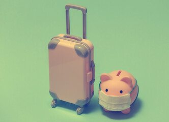 Travel during covid-19. Mini plastic travel suitcase and piggy bank with face mask on blue background.
