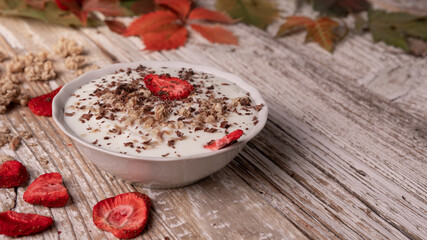the concept of a healthy autumn breakfast. natural yogurt with dehydrated strawberries and muesli on a wooden background top view