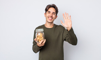 young hispanic man smiling happily, waving hand, welcoming and greeting you. cookies concept