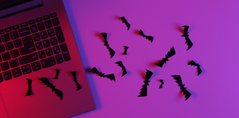 Laptop and Flying paper cut bats in neon blue pink light. Halloween theme