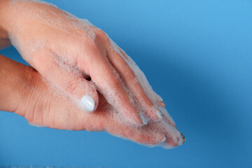 Bubble bath foam in woman's hands. Closeup woman's hand washing with soap on a blue background , selective focus. Practice good hygiene. Hygiene and health protection