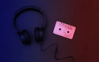 Retro audio cassette and headphones in blue red neon light. Top view