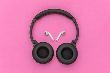 Wireless large stereo headphones and small earbuds on pink background. Top view