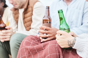 Close up of young people holding beer bottles while enjoying camping in Autumn