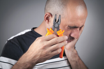 Caucasian man suffering from toothache holding pliers.