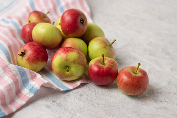 A pile of ripe red and green pure apples on a striped napkin. Harvest of juicy apples on a light background