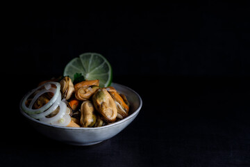 Mussels marinated in vinegar. Seafood appetizer fresh mussels marinated in vinegar and onions in a bowl. Top down view. On a dark background in a spotlight.