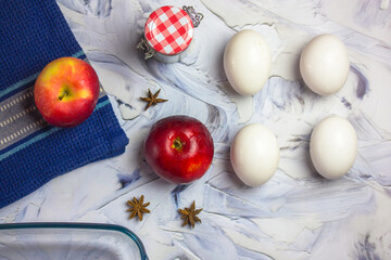 Ingredients for making traditional American apple pie at home for Thanksgiving. Red ripe apples, chicken eggs, aniseed spices, cinnamon sticks on a blue kitchen towel on a white table flatly, top view