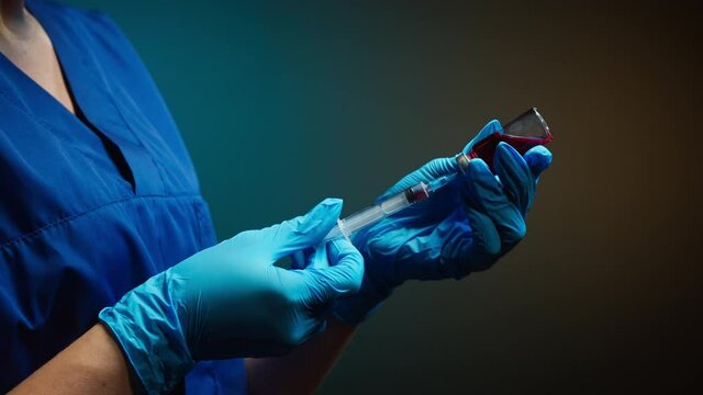 Doctor filling syringe with red solution. Nurse wearing protective gloves showing sample of medicine, vaccination against covid-19, laboratory research concept. Coronavirus vaccine.