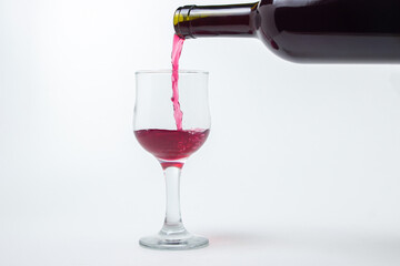 Red wine is poured into a glass from a bottle on a white background. Wine alcoholic drink.