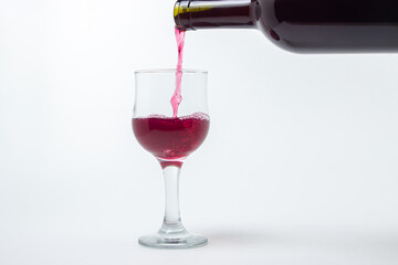 Red wine is poured into a glass from a bottle on a white background. Wine alcoholic drink.