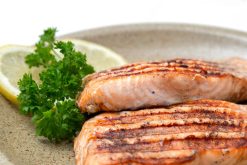 Grilled salmon fillet and lemon slices on a plate. White background. Healthy food. Close up.