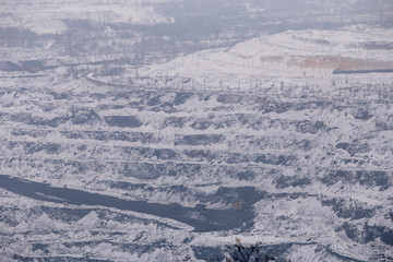 Iron ore quarry horizons covered with snow in winter, mining process in winter in cloudy weather