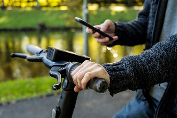 Man holding a phone and using mobile app for rent electronic scooter. Close-up. Modern eco urban transportation.