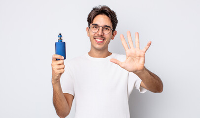 young hispanic man smiling and looking friendly, showing number five. smoke vaporizer concept